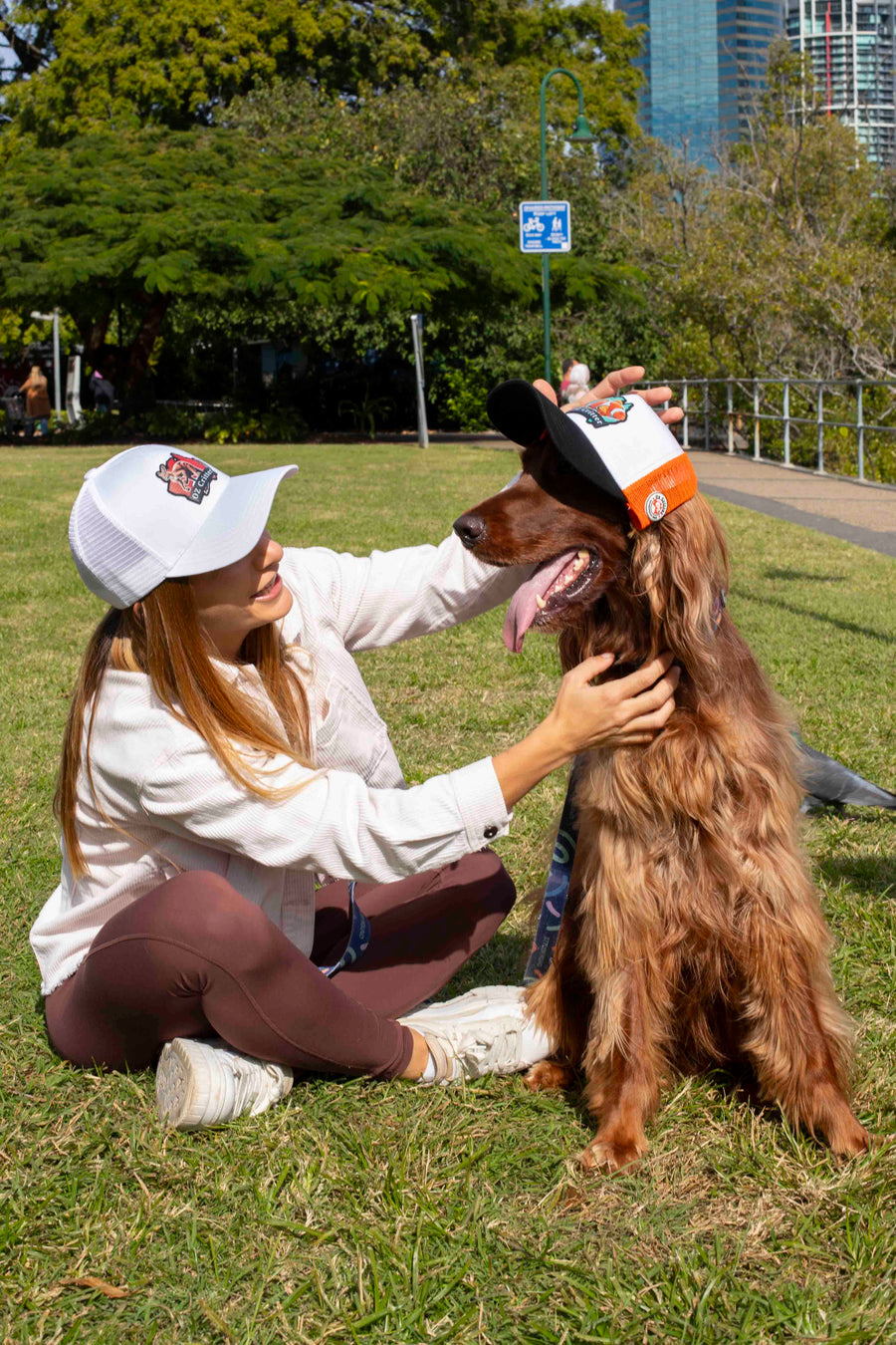 Woman sitting on grass with a dog wearing a cap in an urban park setting