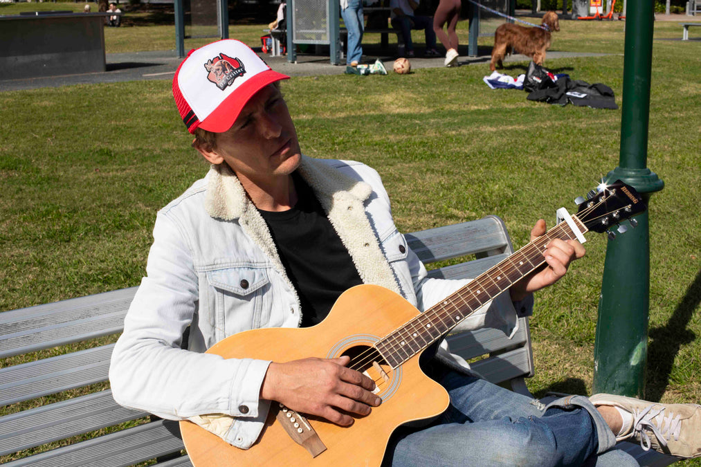 Person playing guitar on a bench in a park wearing OZ Critter cap