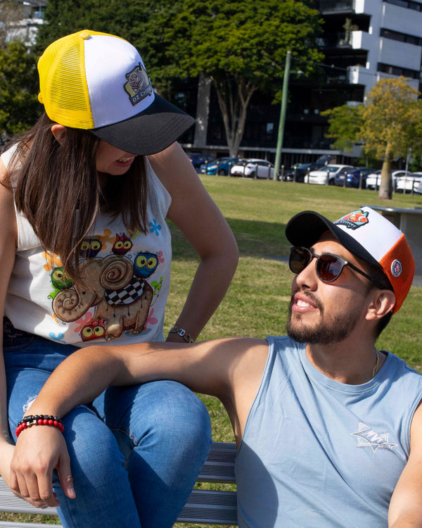 Two people sitting on a bench outdoors with colorful caps and casual clothing.
