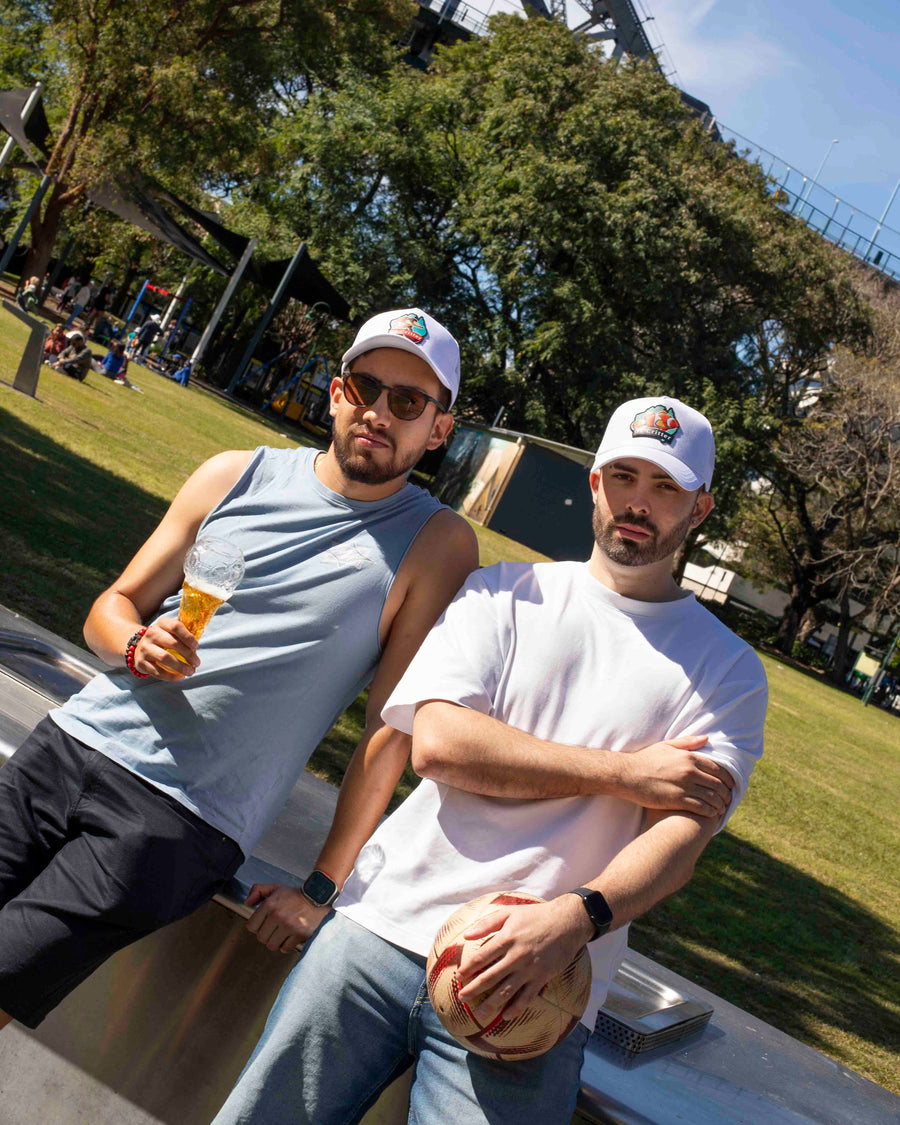 Two men sitting on a truck bed in a park with trees and people in the background.