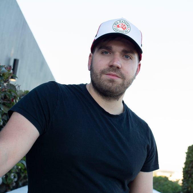 Man wearing a black t-shirt and white trucker cap with a logo outdoors