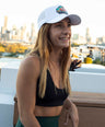 Woman wearing a white fish cap with a logo, sitting on a rooftop with a cityscape in the background