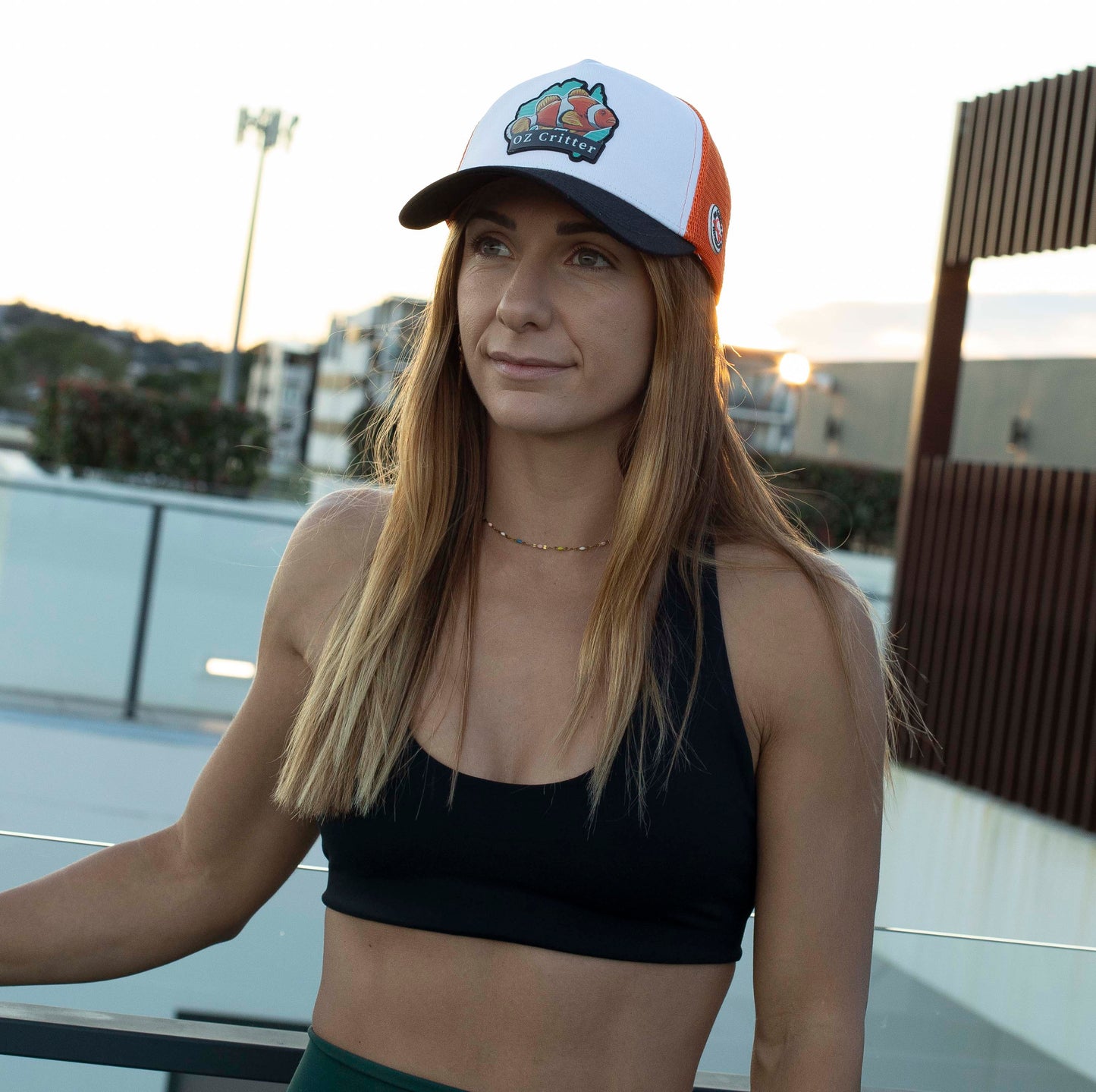 Woman wearing a black sports bra and green shorts with a fish cap, standing outdoors.