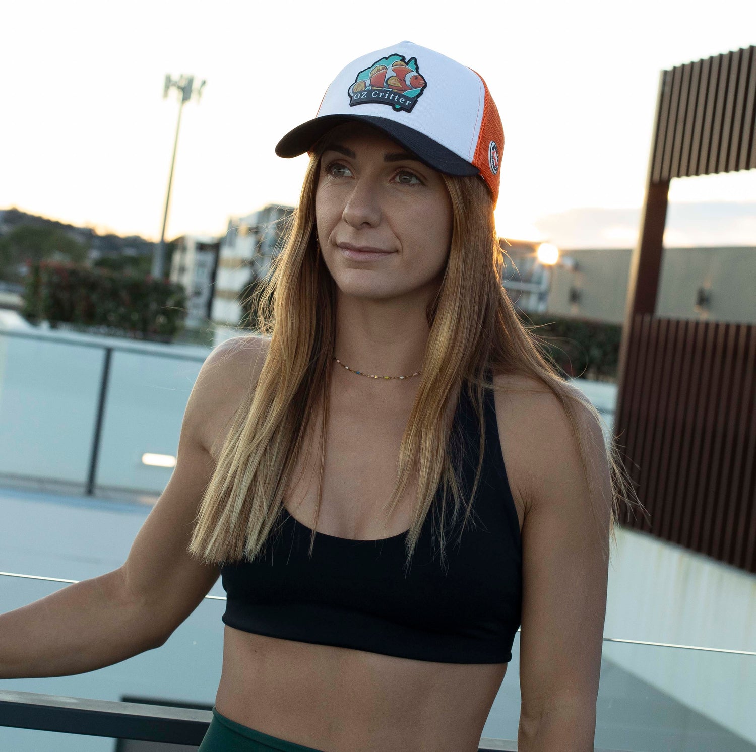 Woman wearing a black sports bra and green shorts with a fish cap, standing outdoors.