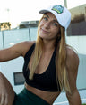 Woman wearing a black sports bra and green shorts with a white Koala cap outdoors.