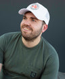 Man wearing a white trucker cap and a green t-shirt against a dark background.