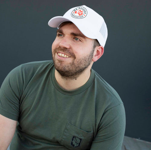 Man wearing a white trucker cap and a green t-shirt against a dark background.