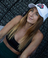 Woman wearing a white kangaroo cap, black sports bra, and green leggings against a dark background.
