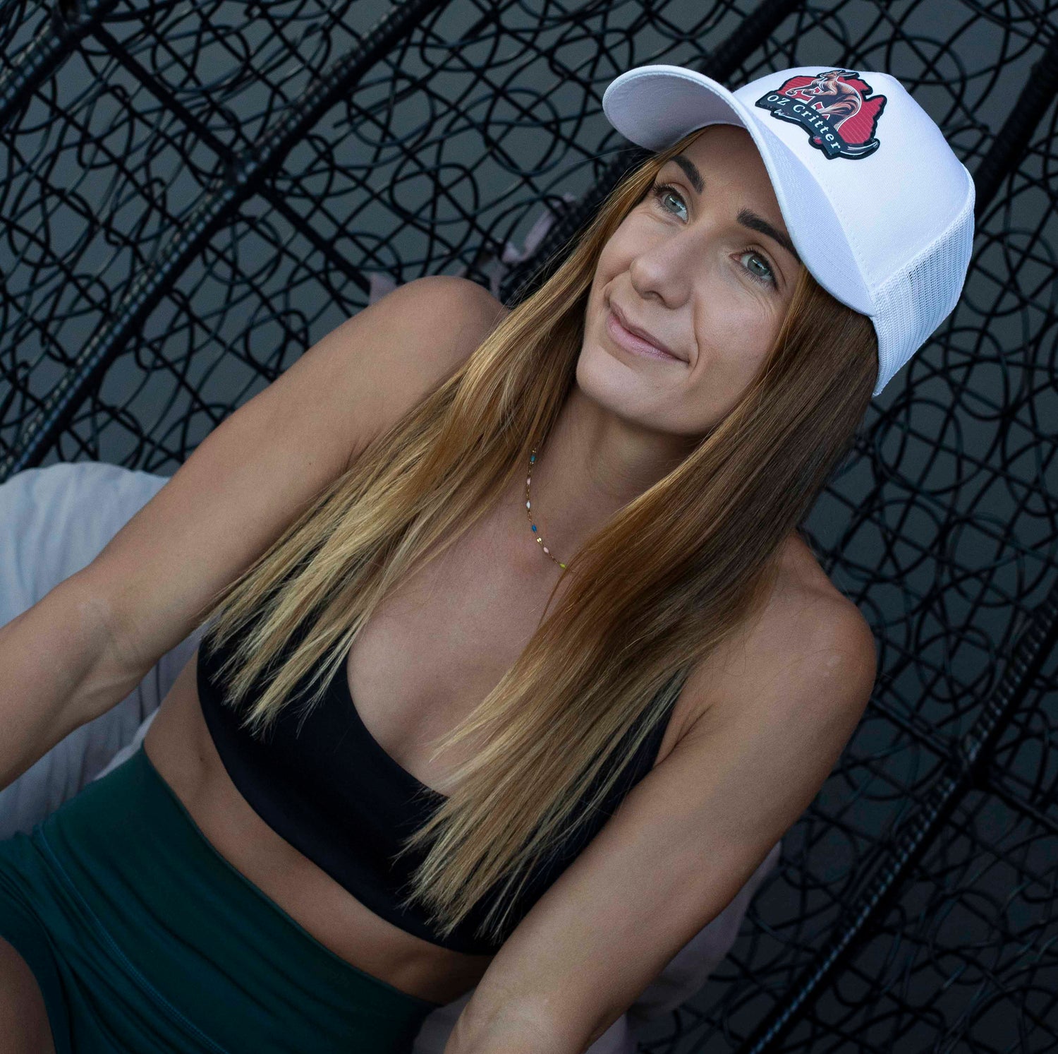 Woman wearing a white kangaroo cap, black sports bra, and green leggings against a dark background.