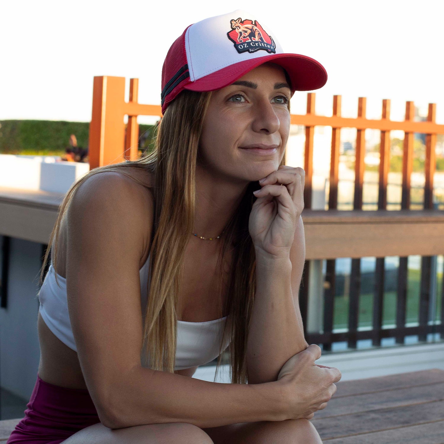 Woman wearing a red and white kangaroo cap, sitting outdoors on a wooden deck.