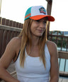 Woman wearing the OZ Critter platypus cap and white tank top on a wooden deck.
