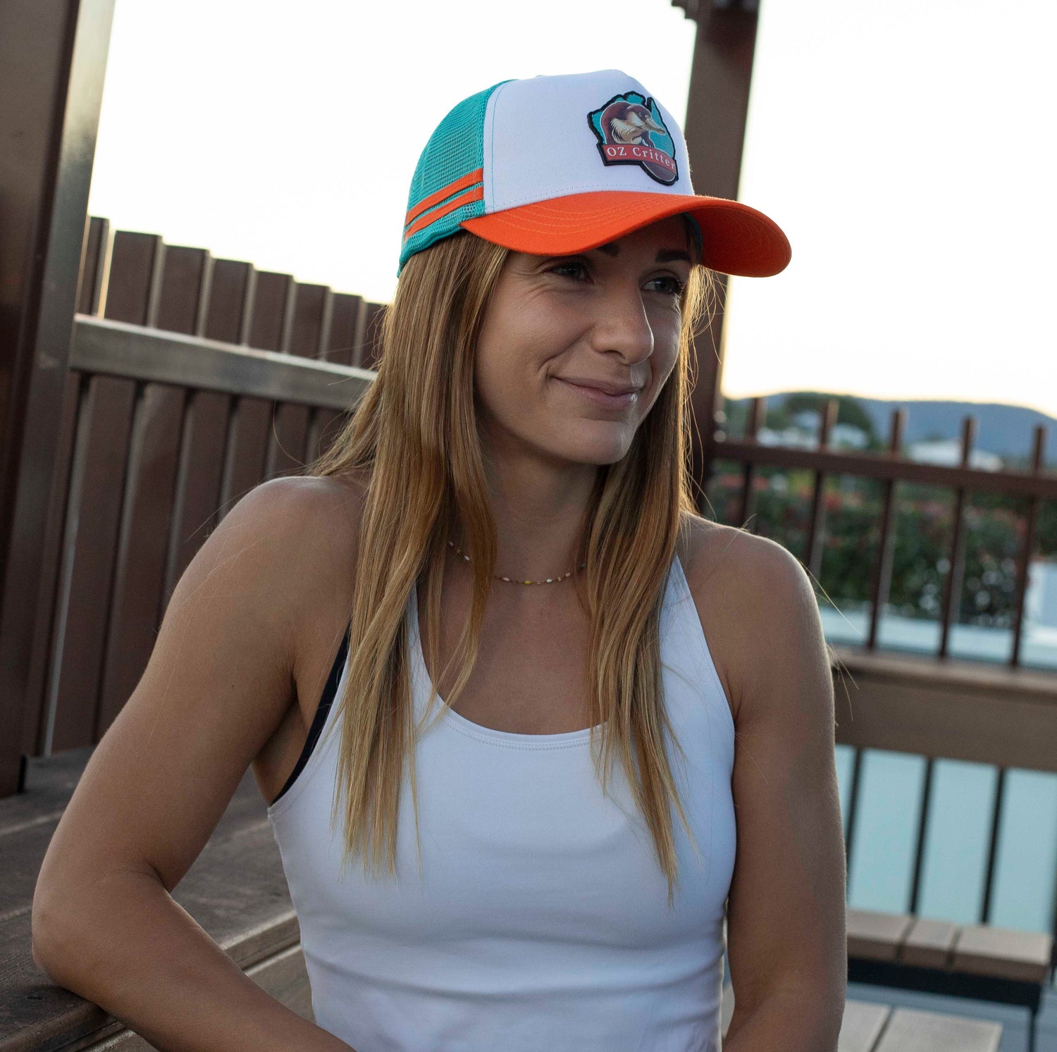 Woman wearing the OZ Critter platypus cap and white tank top on a wooden deck.